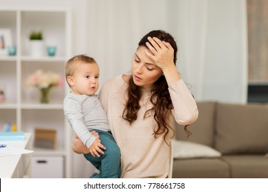 Motherhood, Multi-tasking And Family Concept - Tired Mother Having Headache With Baby Boy At Home