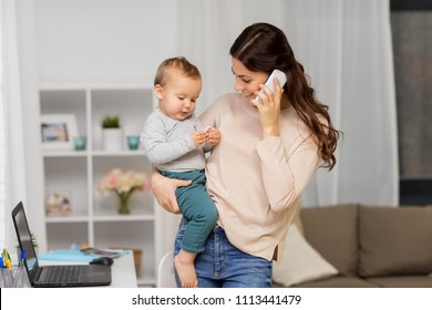 Motherhood, Multi-tasking, Family And Technology Concept - Happy Mother With Baby Calling On Smartphone At Home