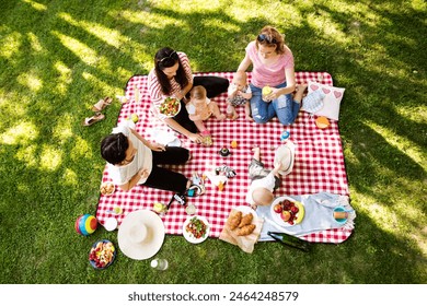 Mothers and babies enjoying group picnic outdoor in park, sitting on picnic blanket and preparing food and drinks. - Powered by Shutterstock