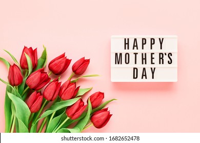 Mothers Day background. HAPPY MOTHERS DAY written in lightbox and bouquet of red tulips on pink background. Top view, copy space for text. Greeting card.