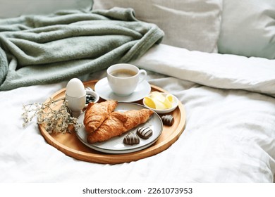 Mothers day breakfast served with love on bed. Coffee, croissant, egg and chocolate hearts on a wooden tray. Natural bed cloth. Also for birthday, valentines or fathers day, copy space, selected focus