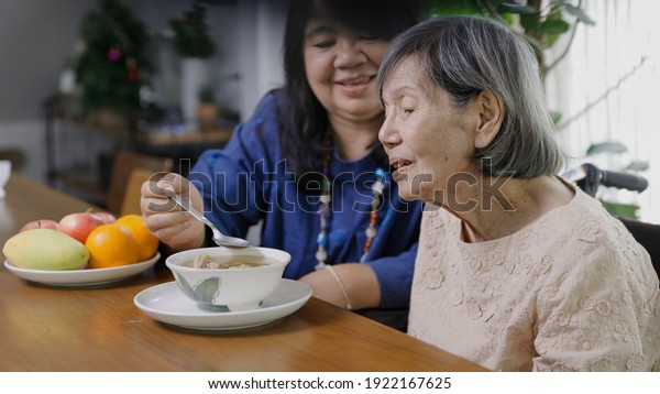 Mother\'s\
Day , Daughter feeding elderly mother with\
soup.