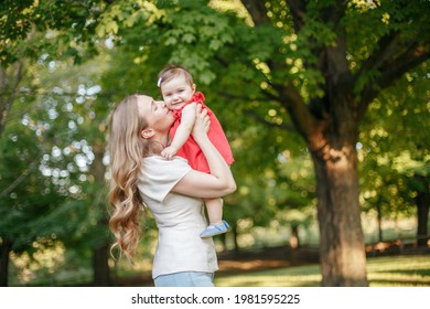 Mothers Day Holiday. Young Smiling Caucasian Mother And Girl Toddler Daughter Hugging In Park. Mom Kissing Child Baby On Summer Day Outdoor. Happy Authentic Family Parenting Lifestyle. 