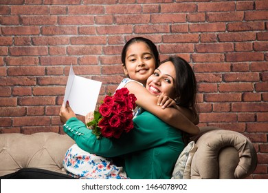 Mother's Day - Indian girl / mother celebrating Mother's day with Rose Flower Bouquet, greeting card while hugging and kissing each other - Powered by Shutterstock