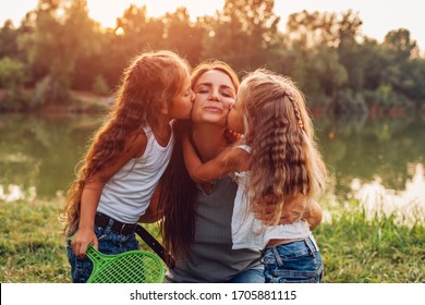 Mother's Day. Kids Kissing Mother On Cheek. Family Walking By In Spring Park By Lake After Playing Badminton.