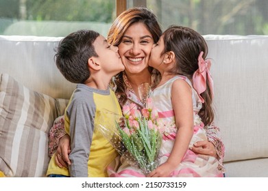 Mother's Day.  Latin mother holds her two children, a boy, and a girl, as they hug and kiss her. - Shutterstock ID 2150733159