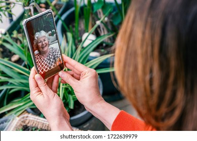 Mother's day lockdown concept: Mother and child laughing during online video call, celebrating this special day. Woman with white hair and glasses smiles into camera. Green leaves in background