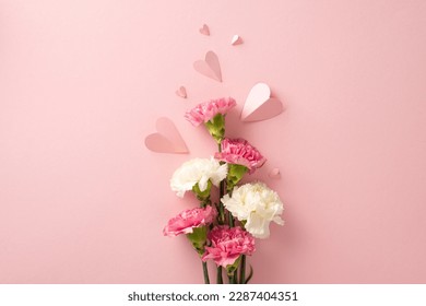 Mother's Day present idea. Top view of carnation flowers and heart-shaped papers on a pastel pink surface