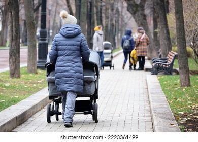 Mothers walking with baby prams on city street at autumn. Woman with stroller for twins in foreground