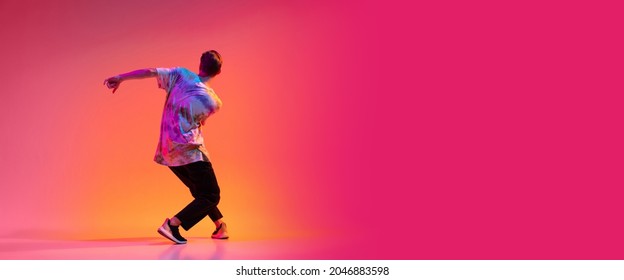 In Motion. Back View Of Active Stylish Man Dancing Hip-hop Isolated Over Colorful Gradient Background In Neon Light. Street Style Dance. Concept Of Dance, Youth, Hobby, Dynamics, Movement, Action, Ad