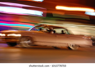 Motion blur car full of people at night, pink finned classic Cadillac from 1950s with blurred streaks from club lights in background - Powered by Shutterstock