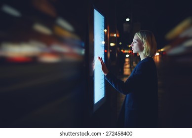 Motion blur effect, female using automated teller machine with big digital screen while standing in night city out-of-focus lights,woman verifies account balance on banking application modern device