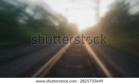 Motion blur effect on train tracks at sunset with sun flares and trees lining the path.