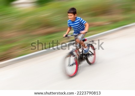 Motion blur image of a boy riding a bike at high speed in a city park