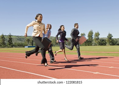 Motion Blur Shot Of Four Business People Running Together On Racing Track