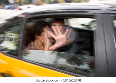 Motion Blur View Of A Couple In Speeding Taxi Through The Window With The Man Blocking The Photographer With His Hand And Woman Shielding Her Face From The Camera.