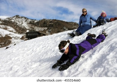 Motion Blur Of A Young Girl (age 6) Sliding On Snow While Here Mother And Sister Watching In Mount Ruapehu, New Zealand. Family Winter Travel Holiday Vacation Concept. Real People. Copy Space