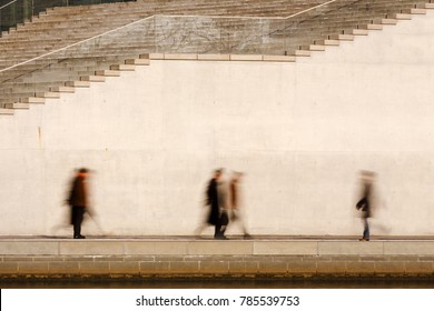 Motion blurred business people walking in front of a bright concrete wall.