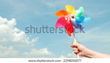 Motion blurred of colorful pinwheel. Woman hand holding colorful plastic windmills on blue sky background. Green energy concept