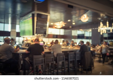 Motion blurred group of people at airport bar. Abstract passengers dinning in, enjoy alcohol beverage and watching sport while waiting for flights