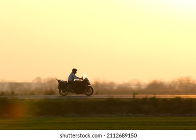 Motion Blurred Image Of Motorcycle Driving Fast On Evening Road