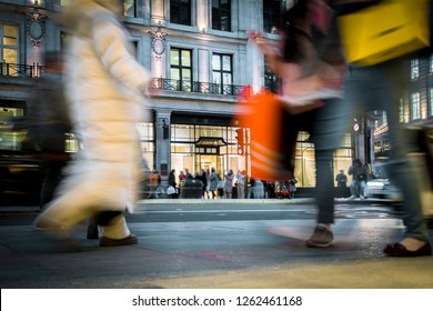 Motion Blurred Night Shoppers With Shopping Bags On Busy High Street