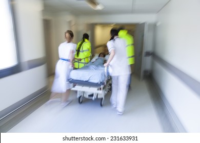 A Motion Blurred Photograph Of A Child Patient On Stretcher Or Gurney Being Pushed At Speed Through A Hospital Corridor By Paramedics, Doctors & Nurses To An Emergency Room