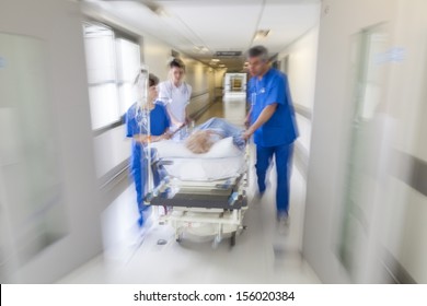 A motion blurred photograph of a patient on stretcher or gurney being pushed at speed through a hospital corridor by doctors & nurses to an emergency room - Shutterstock ID 156020384
