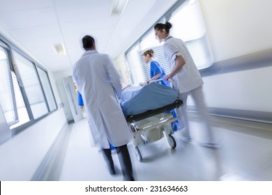 A motion blurred photograph of a patient on stretcher or gurney being pushed at speed through a hospital corridor by doctors & nurses to an emergency room