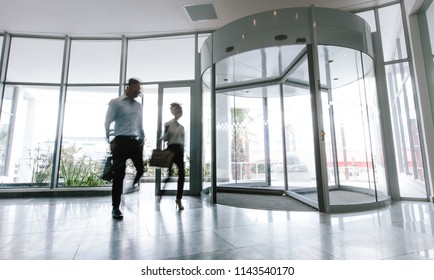 Motion Blurred Shot Of Two Business People Talking Through Modern Office Hallway. People Walking In Office Entrance Hall.