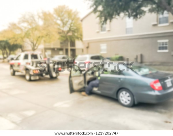 Motion blurred tow\
truck driver towing a damaged car from apartment building complex\
in Texas, America. Insurance theme concept, roadside assistance\
accident support