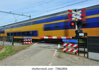 Motion blurred train passing a railroad crossing. Dutch signs warning not to cross and red lights flashing.