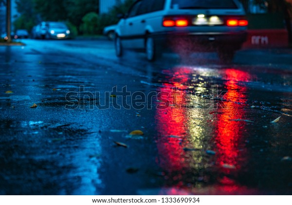 Motion car in rain with selective focus, color\
toned. Night road blurred, in the dark while heavy raining. Back\
light of car on raining road, light reflected on road. View from\
the level of asphalt
