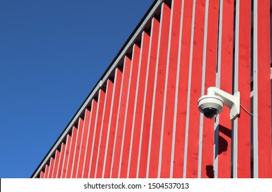 A Motion Detecter Which Lights A Lamp Attached To A Red Building. The Sun  Is Shining And The Sky Is Blue. The Contrast Of Colours Is Beautiful. 