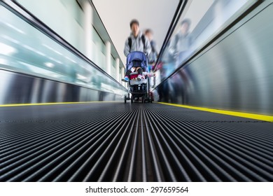 Motion of moving modern escalator way in the airport with a father holding a perambulator with his child sitting in