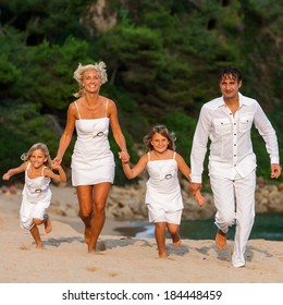 Motion Portrait Of Young Family Running Towards Camera On Beach.