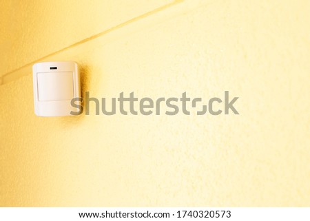 Motion sensor or detector for security system on a yellow wall indoors. Place for text.