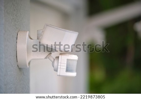 Motion sensor with light detector mounted on exterior wall of private house as part of security system