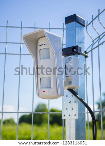 Motion sensor on open protected area. Installed on the fence and connected to the security system with wires. Multifunctional microwave detector. Outdoor guard. Concept of personal or object security.