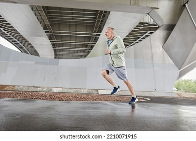 Motion Shot Of Active Mature Man Running Against Concrete Background In Urban City Setting, Copy Space