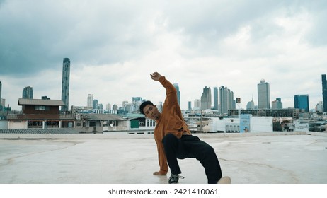 Motion shot of B-boy dance performance by professional street dancer at rooftop with sky scrapper, city view. Attractive asian hipster show energetic footstep. Outdoor sport 2024. Endeavor.