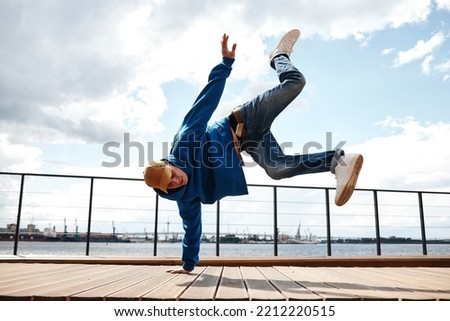 Motion shot of young man doing breakdance stunts outdoors against sky, copy space