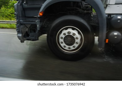 Motion-blurred Photo Of The Wheels In Rapid Rotation Of A Tractor Trailer Driving At High Speed By Rainy Weather On A Wet Road And Projecting Splash And Drops Of Water On The Asphalt Of The Motorway