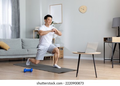 Motivated athletic handsome middle aged asian man exercising at home, training on yoga mat, using laptop, watching online fitness class, copy space. Workout plan for men concept - Powered by Shutterstock