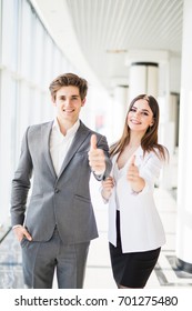 Motivated businessman and woman giving a thumbs up gesture of approval and success as they pose side by side giving the camera big friendly