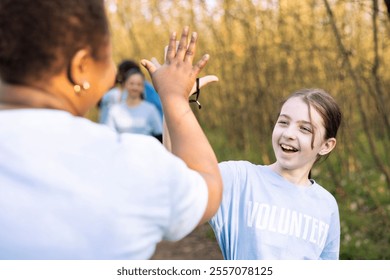 Motivated cheerful child sharing high five with her friends, finishing litter cleanup of the woodland and saving the ecosystem. Satisfied volunteers congratulating and praising each other. - Powered by Shutterstock