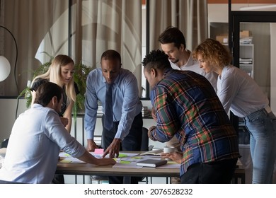 Motivated concentrated young teammates gathered at table, discussing sales data statistics or marketing research results, analyzing paper reports or documents together in modern boardroom. - Shutterstock ID 2076528232
