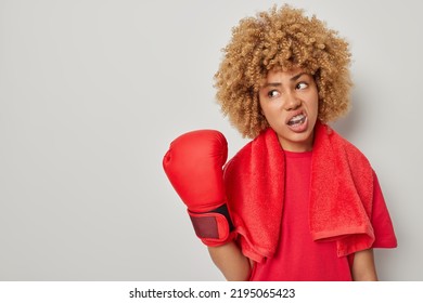 Motivated Curly Female Boxer Wears T Shirt Boxing Gloves Towel Around Neck Mouth Guard Rests Ater Workout Isolated Over Grey Background Empty Space For Your Advertising Content. Sport Concept