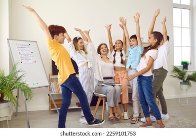 Motivated elementary school students and their teacher support each other during creative school lesson. Joyful female teacher and schoolchildren actively raise their hands together in classroom. - Powered by Shutterstock