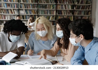 Motivated Focused Happy Millennial Diverse Students In Facial Masks Sitting Together At Table, Preparing For Exams Or Making College Assignments, Taking Covid 19 Coronavirus Precautions In Library.